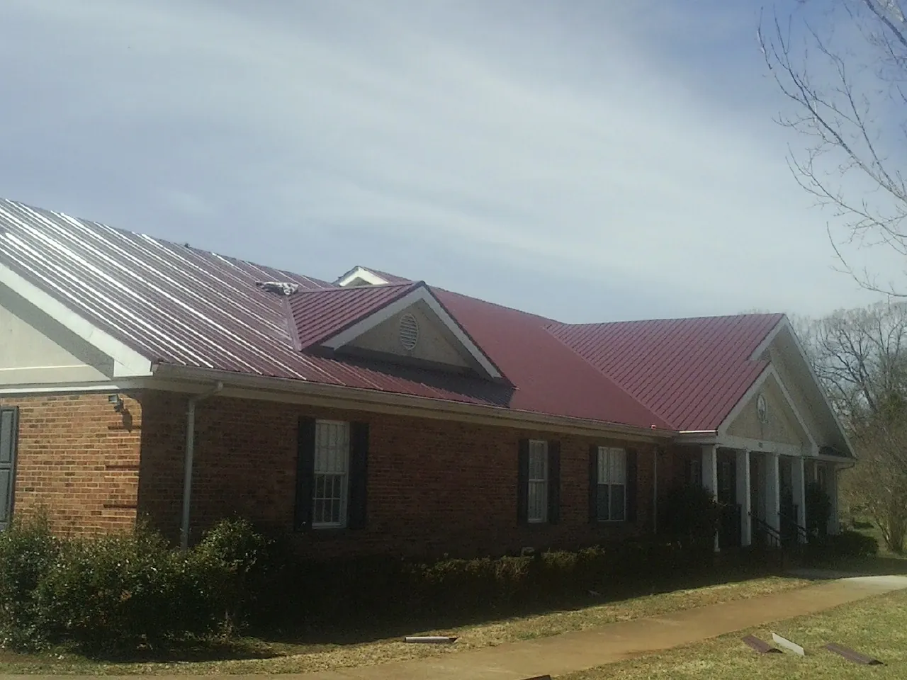 Red metal roof with gabled entries on a long brick building, from a Hail Damage Roof Repair job in Bohemia