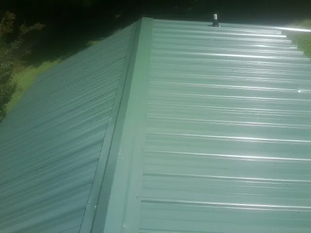 New green metal panels meeting at the ridge of a roof — Flat Roof Repair work by our crew in Bohemia