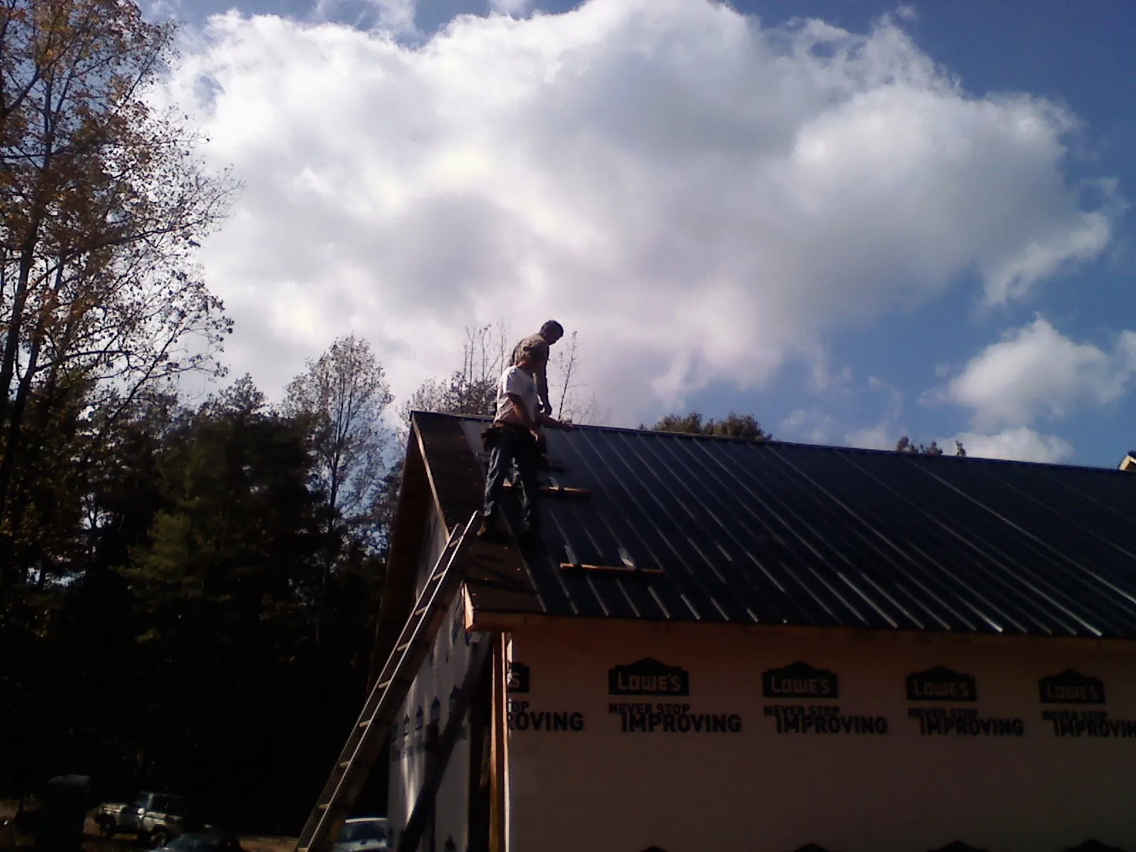 Roofer fastening dark metal panels high against a cloudy sky, from a Roof Inspection job in Bohemia