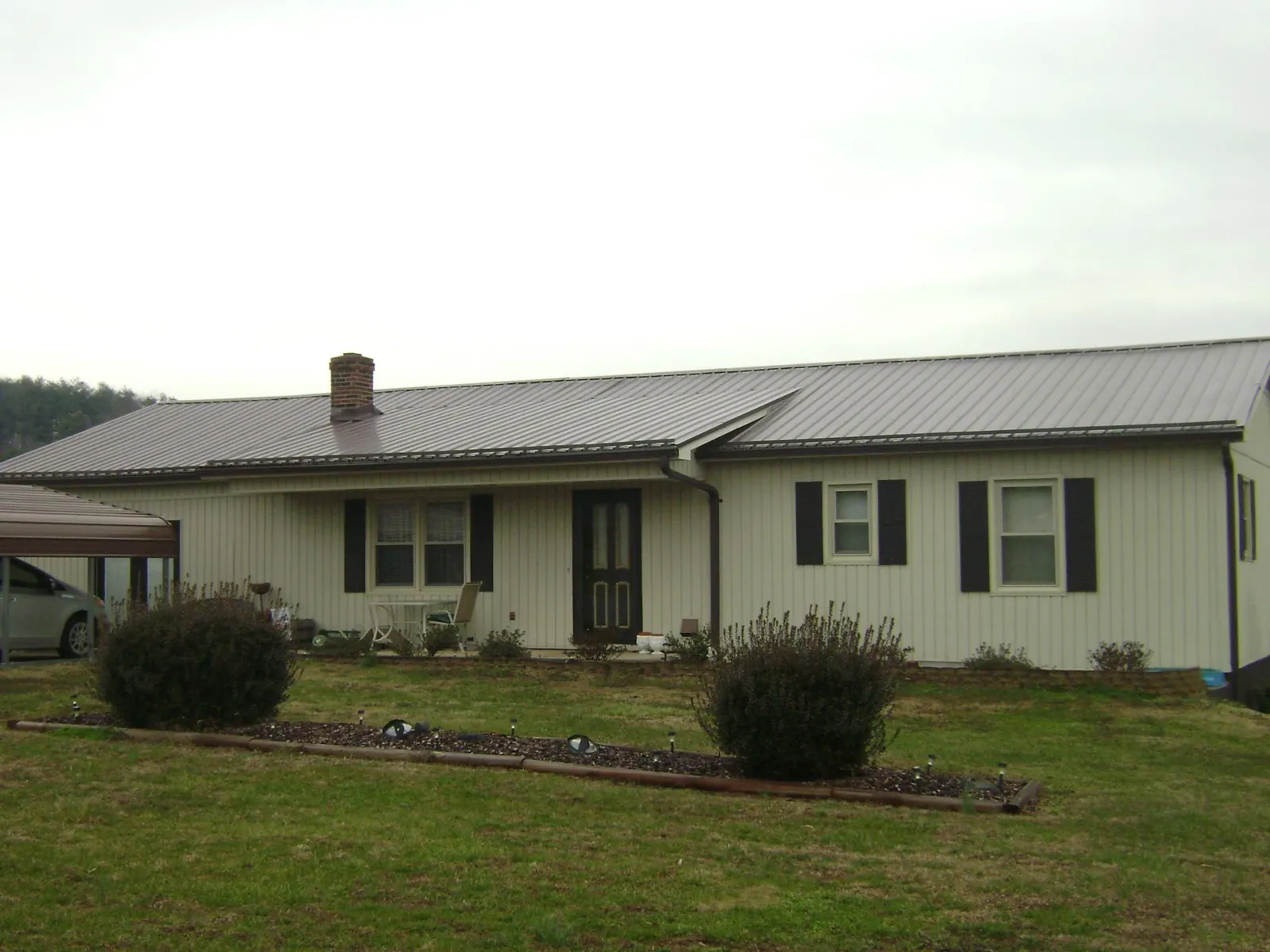 Brown metal roof on a cream sided ranch home with a brick chimney in Bohemia