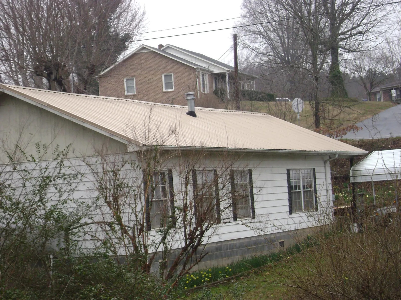 Tan metal roof on a white sided house set into a hillside — Commercial Roofing by Roofing Brothers in Bohemia