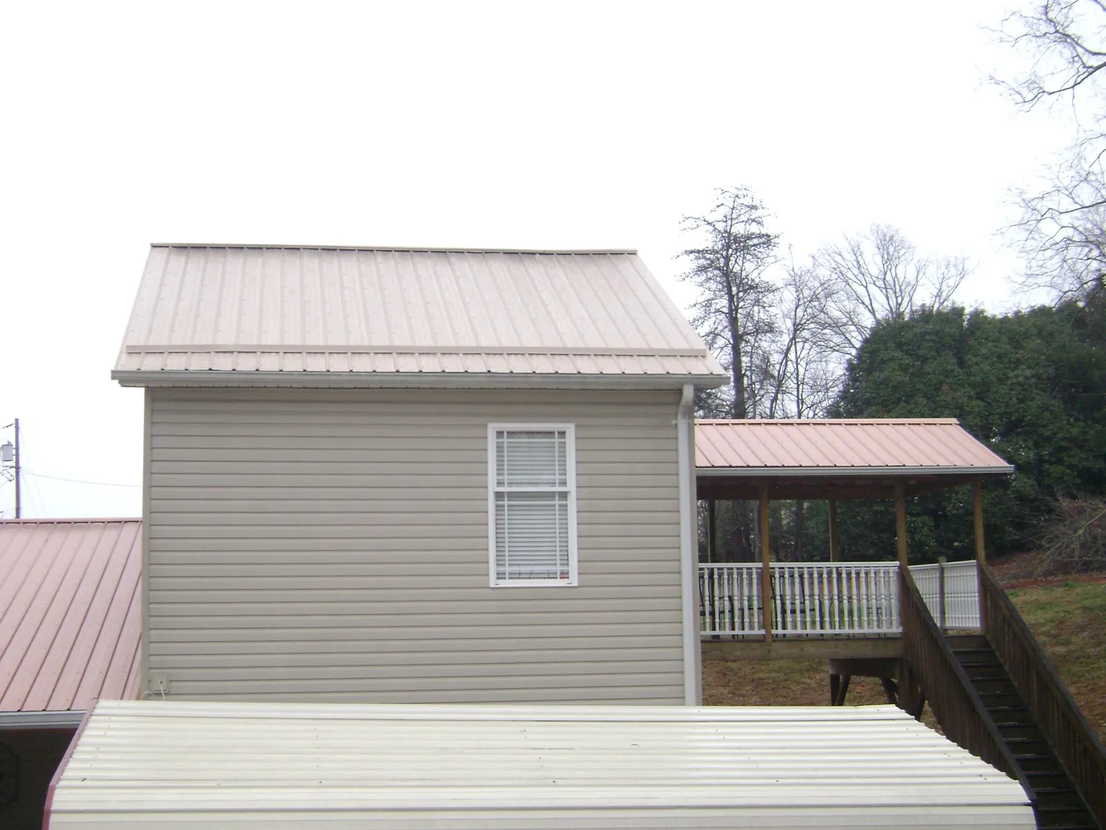 Tan metal roofs on a two story addition and attached porch, from a Roof Replacement job in Bohemia